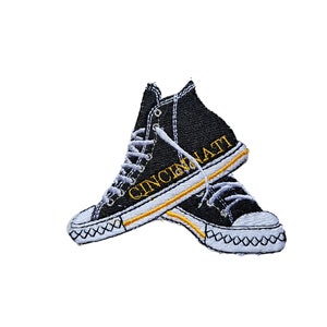 Op de afbeelding: Zwarte en witte geborduurde patch van een paar hoge sneakers met een gele omtrek en het woord "CINCINNATI" erop.