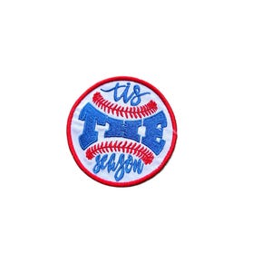 May include: A circular embroidered patch featuring a white baseball design with red stitching. The text 'tis THE season' is stitched in blue across the center. The patch is finished with a bold red stitched border around the entire circumference.