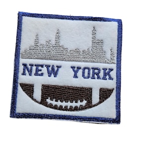 May include: White embroidered patch with a silver outline of the New York City skyline and the text "NEW YORK" in blue. A brown football is below the skyline.