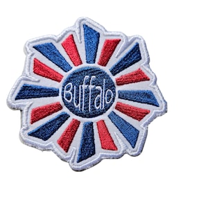 May include: A white, blue, and red embroidered patch in the shape of a sunburst with the word "Buffalo" in the center.