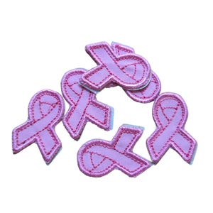 May include: A collection of six pink ribbon patches, embroidered with a darker pink outline. The patches are arranged on a white background. The ribbons are a symbol of breast cancer awareness.