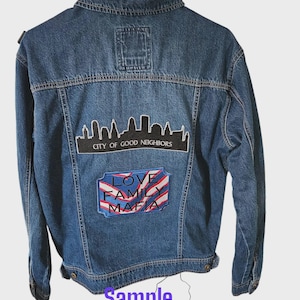May include: A blue denim jacket featuring a cityscape patch and a patch with the words "LOVE FAMILY MAFIA". The jacket has a classic design with button closures and pockets. The text "Sample Only" is at the bottom.