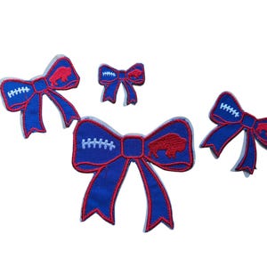 May include: Four blue and red decorative bows. The bows have a football design with white stitching and a red buffalo logo. The bows are in various sizes and are set against a white background.