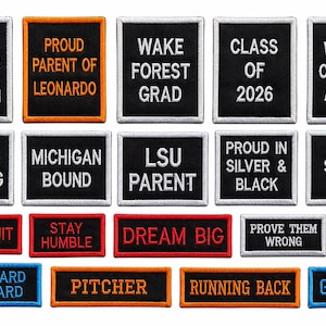 May include: A collection of embroidered patches with various phrases and text. The patches are rectangular, with black backgrounds and white or colored text. Some patches include phrases like "Texas Strong," "Dream Big," and "QB."