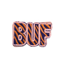 May include: Embroidered patch with the word "BUF" in a bubble letter style. The letters are navy blue with orange tiger stripes, outlined in pink, and set against a white background.