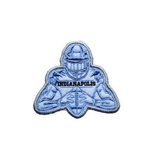 Op de afbeelding: Een geborduurde patch in blauw en wit met een American footballspeler met een helm en het woord "INDIANAPOLIS" in zwarte tekst.