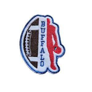 Puede incluir: Parche bordado azul y blanco con un balón de fútbol y una silueta roja de una persona. La palabra "BUFFALO" está escrita verticalmente en el parche.
