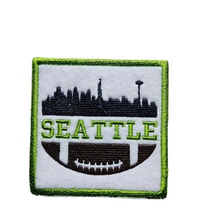May include: Green and white embroidered patch with a black silhouette of the Seattle skyline and a football. The text "SEATTLE" is embroidered in green.
