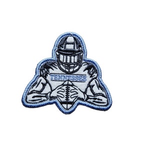 May include: Embroidered patch featuring a football player in a helmet and uniform, holding a football. The player is in a defensive stance. The patch is outlined in blue and has the word "TENNESSEE" in white lettering.