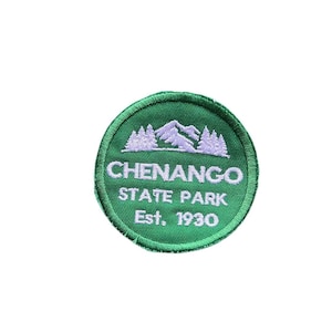 May include: A circular embroidered patch with a green background featuring a white mountain and pine tree graphic at the top. The text reads CHENANGO STATE PARK Est. 1930 in white capital letters. The patch has a stitched green border edge.