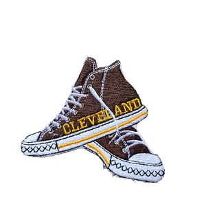 May include: Brown embroidered patch of a pair of high-top sneakers with yellow stitching and the word "CLEVELAND" on the side.