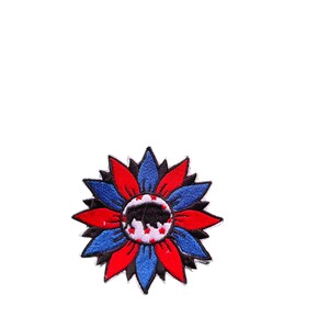 May include: A colorful embroidered patch in the shape of a sunflower. The petals are red, blue, and black. The center features a black buffalo silhouette with white stars on a white background. The patch is likely for clothing or accessories.