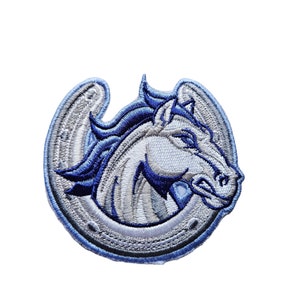 May include: An embroidered patch featuring a white horse's head inside a blue horseshoe. The horse's mane and tail are blue, and the horseshoe has a silver outline.