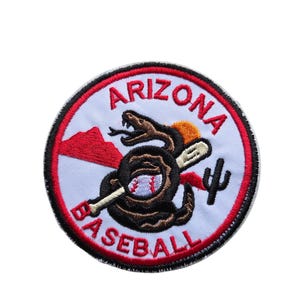 May include: Circular patch with a white background, red border, and black stitching. The patch features the words "ARIZONA BASEBALL" in red. A brown snake wraps around a baseball bat, with a red mountain and cactus.
