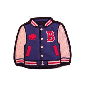 May include: Embroidered patch of a blue varsity jacket with light pink sleeves. The jacket features a red letter "B" and a red buffalo logo. Red and white striped details are on the collar, cuffs, and pockets. The patch has a black border.
