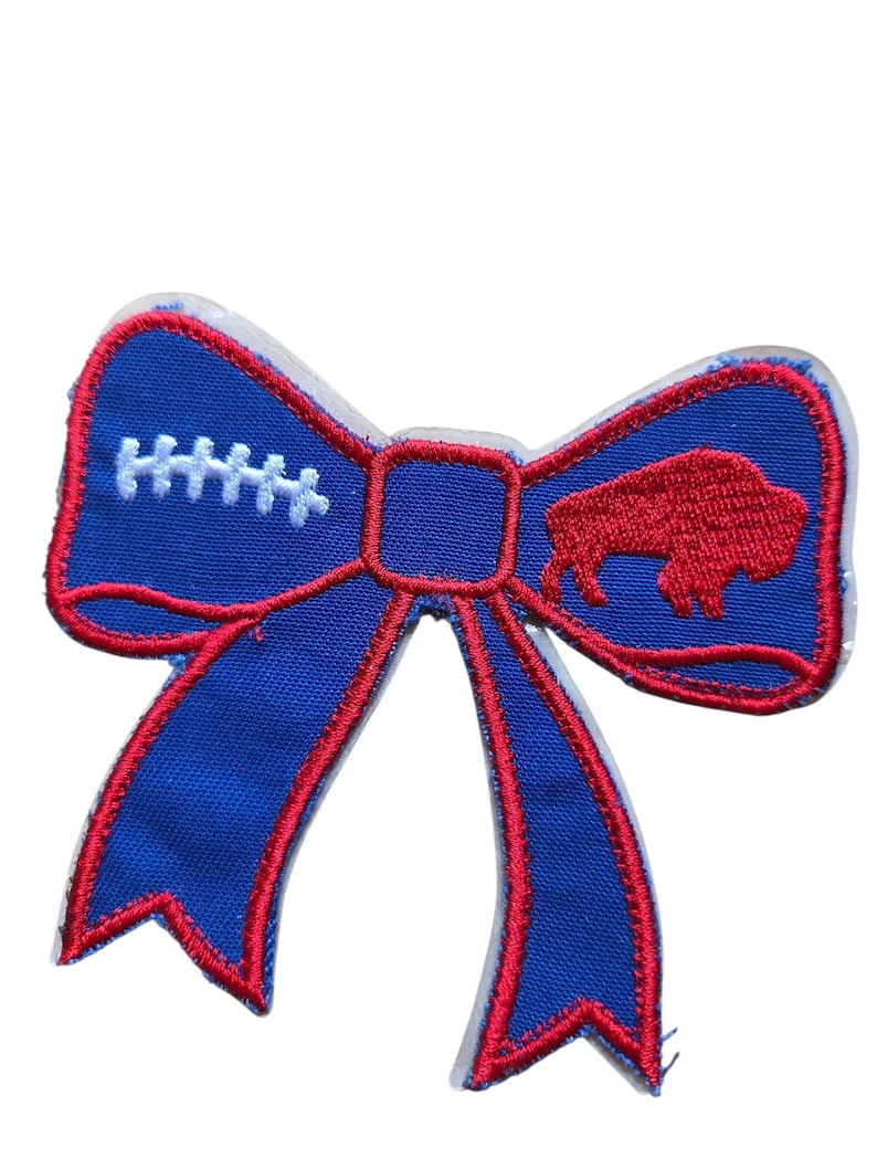 May include: A blue bow-shaped patch with red trim. The bow features a football design on one side and a red buffalo logo on the other. White stitching details the football shape. The patch is likely for sports fans, possibly for the Buffalo Bills.