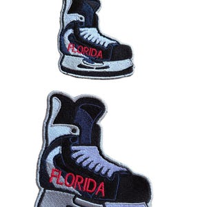 May include: Two embroidered patches shaped like ice skates. The skates are black, white, and light blue, with the word "FLORIDA" in red. The patches have a detailed, stitched design, suitable for application on clothing or accessories.