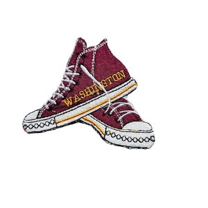 Op de afbeelding: Bordeauxrode geborduurde patch van een paar hoge sneakers met witte veters en een gele streep. Het woord "WASHINGTON" is in geel geborduurd op de zijkant van de schoen.