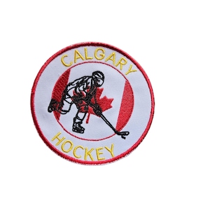 May include: A circular embroidered patch featuring a white background with a red border. The center displays a black silhouette of a hockey player over a red maple leaf. The text CALGARY is arched above and HOCKEY is arched below in yellow.