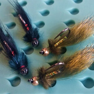 May include: Four fly fishing lures with black, green, and brown feathers. The lures have a metallic gold bead and a red accent.