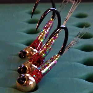 May include: Three colorful fly fishing lures with gold beads and iridescent bodies. The lures are tied on black hooks and have white fibers.