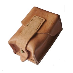 Peut inclure: Une petite pochette en cuir marron clair avec une fermeture à rabat et un bouton pression en métal. La pochette est faite d'un cuir souple et doux et a un aspect rustique et vintage.