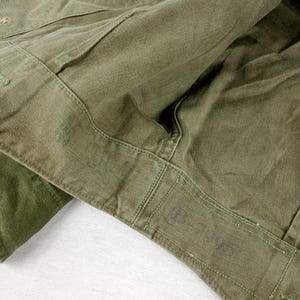 May include: Close-up of the inside of a green military jacket. The jacket has a sewn-in label that reads "U.S. ARMY".