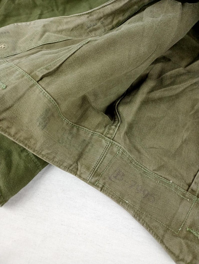 May include: Close-up of the inside of a green military jacket. The jacket has a sewn-in label that reads "U.S. ARMY".