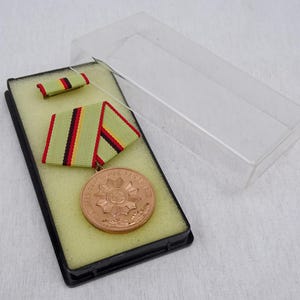 May include: A bronze medal with a starburst design and the text "Bundeswehr" in a black display case with a green and red ribbon.