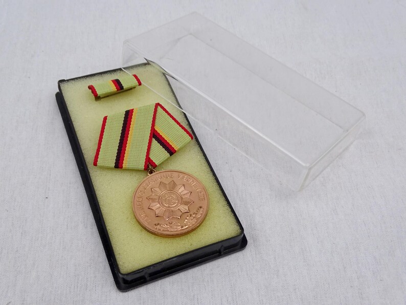 May include: A bronze medal with a starburst design and the text "Bundeswehr" in a black display case with a green and red ribbon.