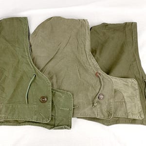 May include: Three olive green canvas hooded vests with drawstrings and buttons.