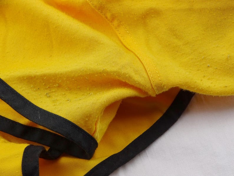 Pu&ograve; includere: Primo piano di pantaloncini gialli con finiture nere. I pantaloncini sono realizzati in un tessuto strutturato e hanno un design semplice e sportivo. Le finiture nere delineano i bordi dei pantaloncini.