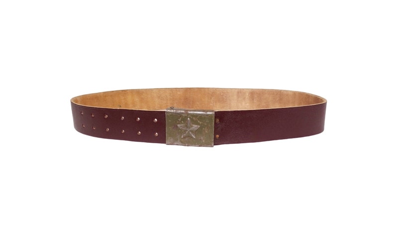 May include: A dark brown leather belt with a metal buckle featuring a five-pointed star. The belt has a tan leather lining and rows of small holes for adjusting the fit.