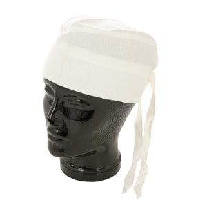 May include: A white, cloth head covering, possibly a surgical cap or a chef's hat, is displayed on a black mannequin head. The cap is tied at the back with two long, thin fabric ties. The fabric appears to be a lightweight cotton or linen.