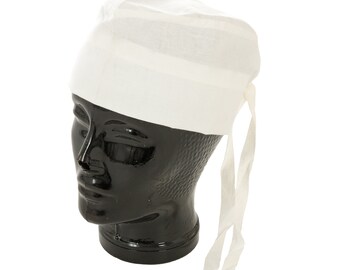 May include: A white, cloth head covering, possibly a surgical cap or a chef's hat, is displayed on a black mannequin head. The cap is tied at the back with two long, thin fabric ties. The fabric appears to be a lightweight cotton or linen.
