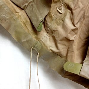 May include: Close-up of a brown canvas bag with a drawstring closure and green plastic buckles. The bag is folded and has a worn appearance.
