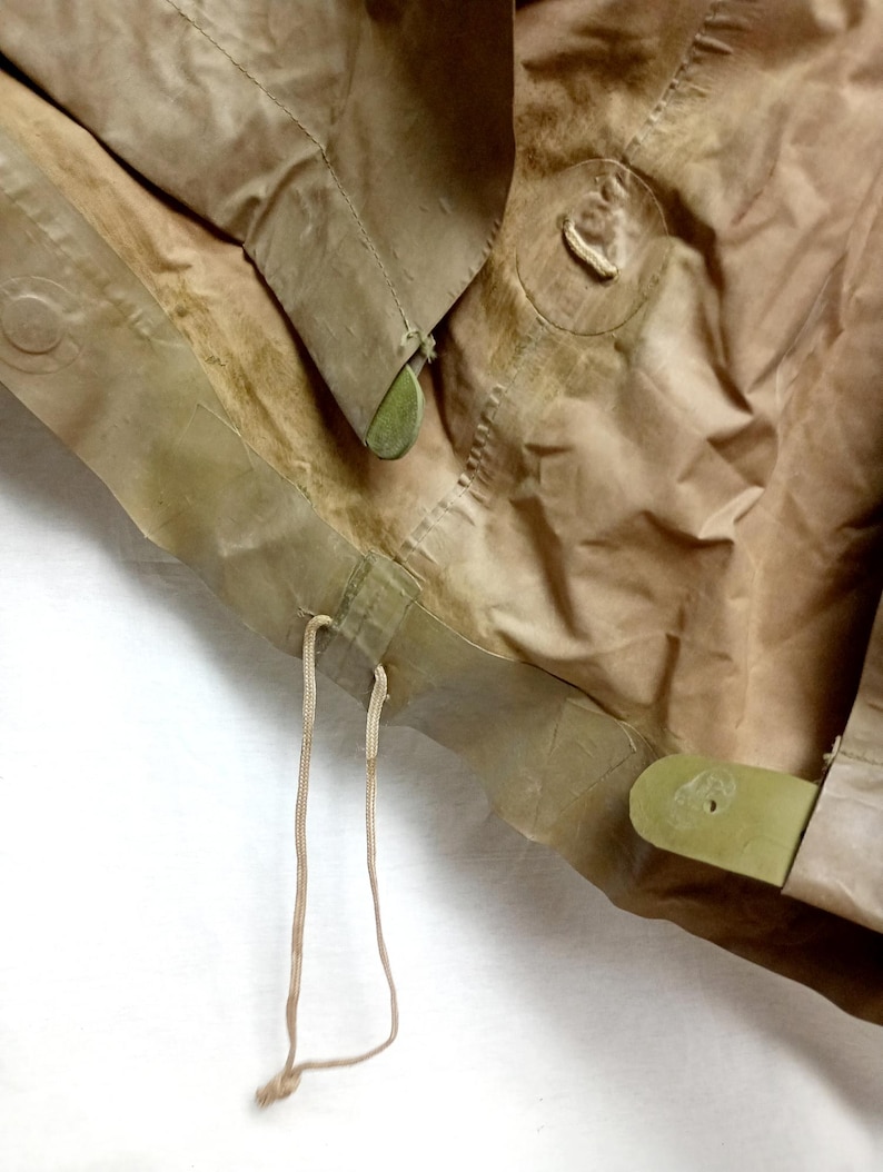 May include: Close-up of a brown canvas bag with a drawstring closure and green plastic buckles. The bag is folded and has a worn appearance.