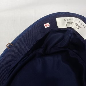 Pu&ograve; includere: Un cappello blu navy con fodera in raso blu scuro. Il cappello ha un bordo in gros-grain e una piccola etichetta con il numero "55". Un'etichetta all'interno recita "Line Daniel PARIS".