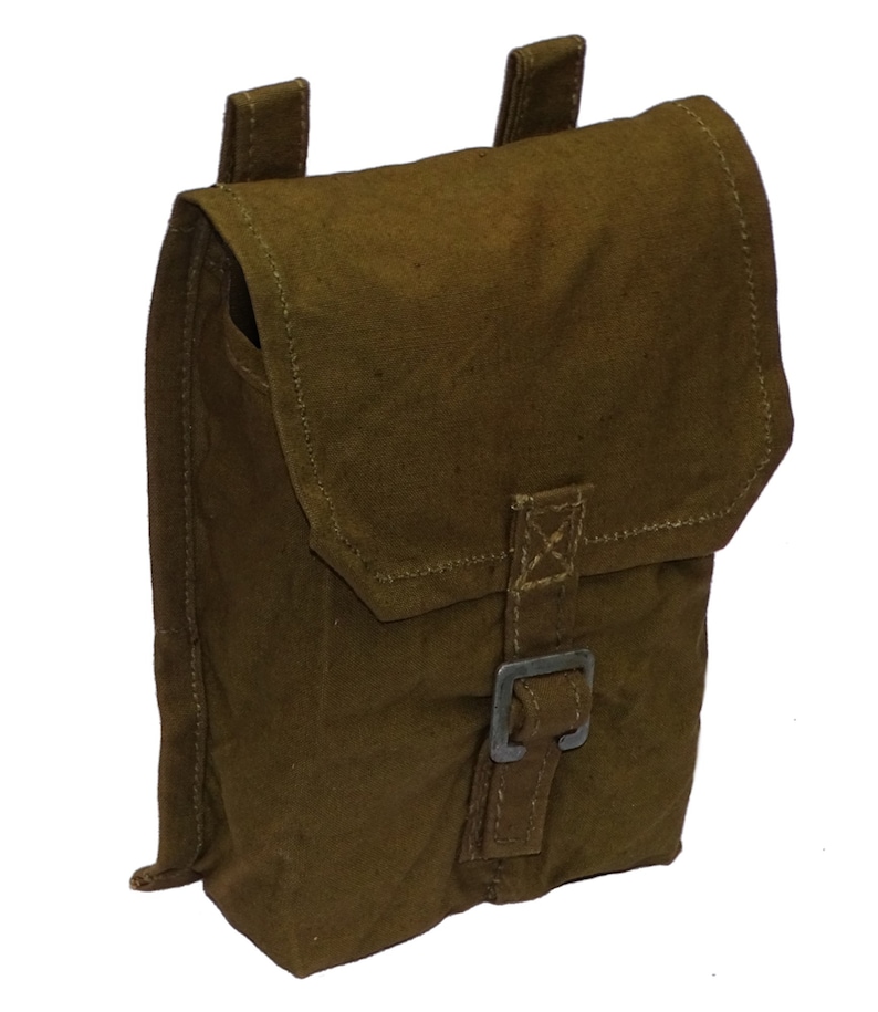 May include: Olive green canvas pouch with a flap closure and a metal buckle. The pouch has two loops on the back and is designed to be worn on a belt or attached to other gear. The stitching is visible and the overall design is simple and functional.