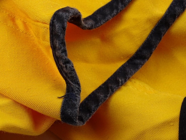 Pu&ograve; includere: Primo piano di tessuto giallo con rifinitura grigio scuro. La rifinitura &egrave; un materiale morbido e vellutato. Il tessuto &egrave; piegato, mostrando la consistenza e il contrasto cromatico tra giallo e grigio.