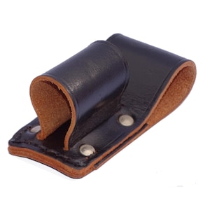 Może przedstawiać: Czarny skórzany uchwyt na narzędzia z brązową skórzaną podszewką i srebrnymi nitami. Uchwyt ma pętlę do mocowania do paska.