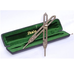 May include: A silver drafting compass with a green velvet lined case. The compass has a scale marked in millimetres and inches. The case has the word "J.Kala" printed on it.