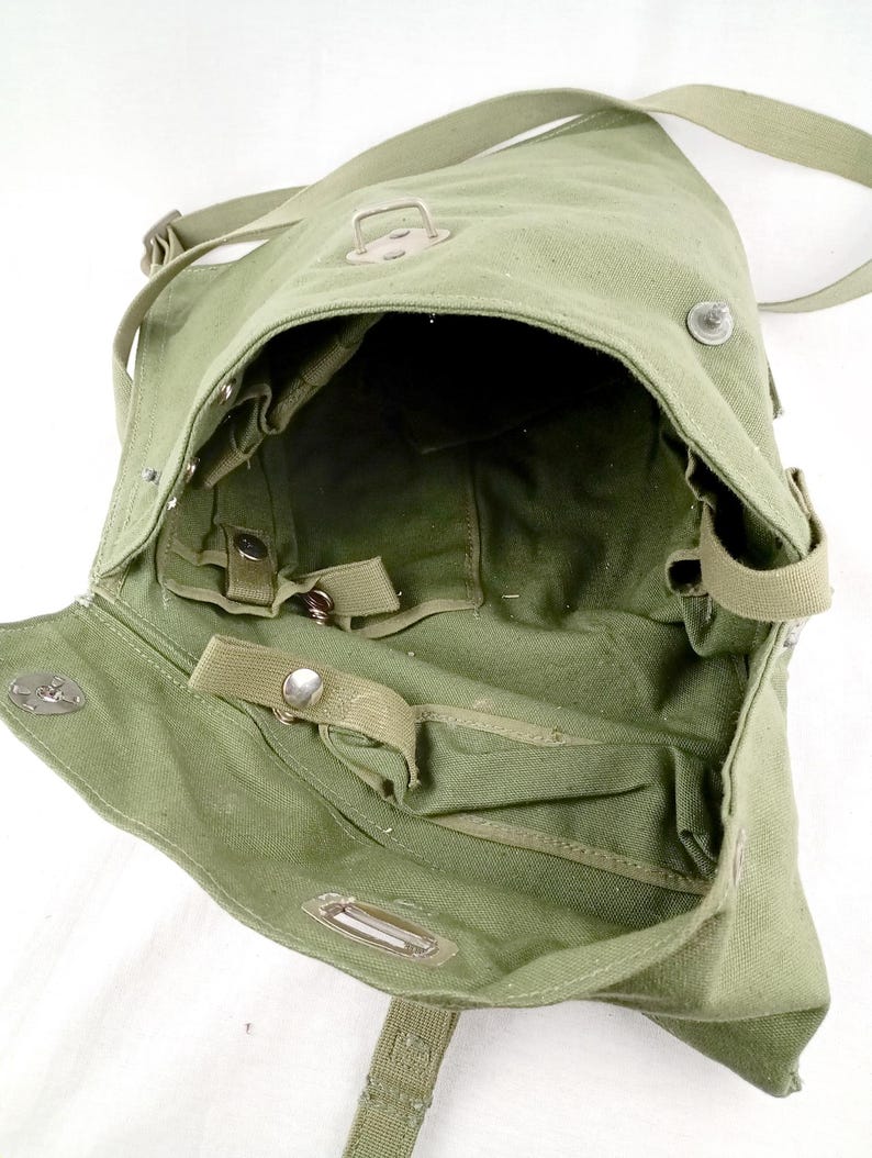 May include: A green canvas military-style shoulder bag with a flap closure and multiple straps and buckles. The bag is open and the interior is visible.