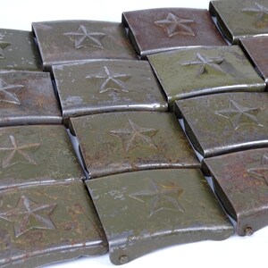 May include: A pile of 15 vintage metal belt buckles with a star design. The buckles are a dark green color with rust spots and are arranged in a staggered pattern.