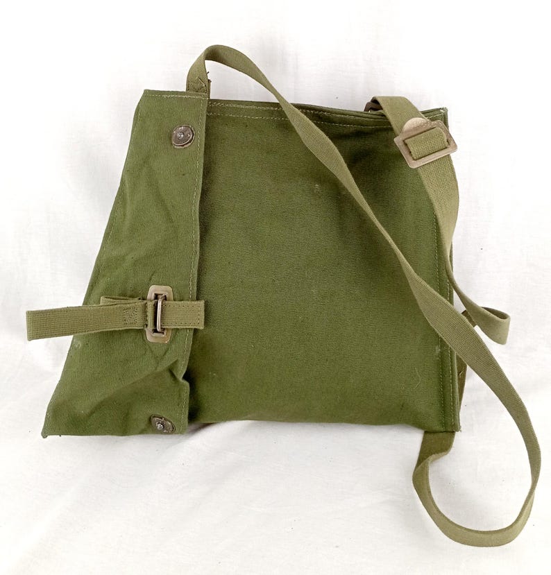 May include: A green canvas bag with a long strap and a buckle closure. The bag has a flap that folds over and is secured with a button.