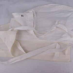 May include: Several off-white fabric caps with attached ties are arranged on a white surface. One cap has the number "2" printed in blue, and another has the number "55" printed in black. The caps are folded and layered.