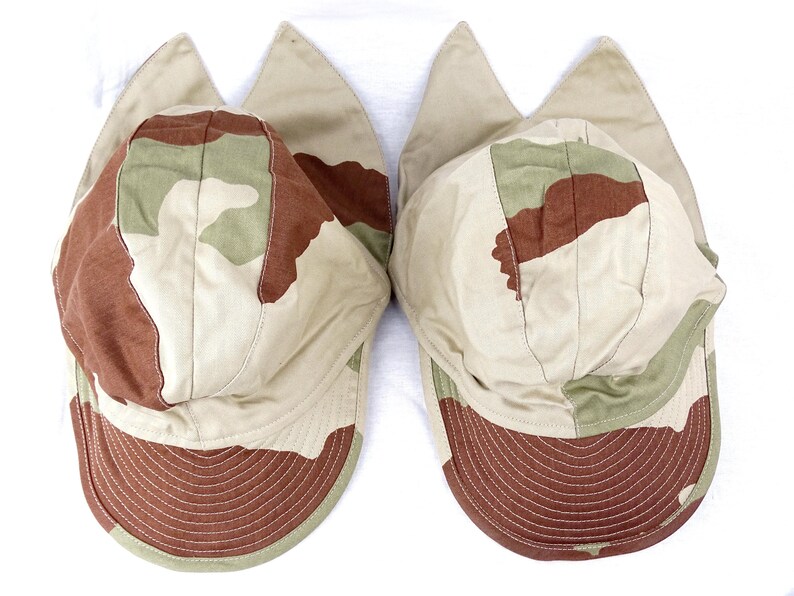 May include: Two camouflage-patterned baseball caps with ear flaps. The caps are beige, brown, and green with a brown brim.