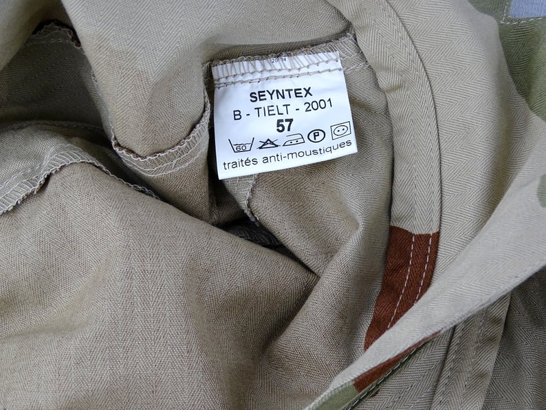 May include: A beige fabric label with the text "SEYNTEX B - TIELT - 2001 57" and symbols for washing instructions. The label also says "trait&eacute;s anti-moustiques".