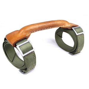 Peut inclure: Une poignée en cuir marron avec deux sangles en toile verte et des boucles argentées. Les sangles sont enroulées autour de la poignée et fixées avec les boucles.