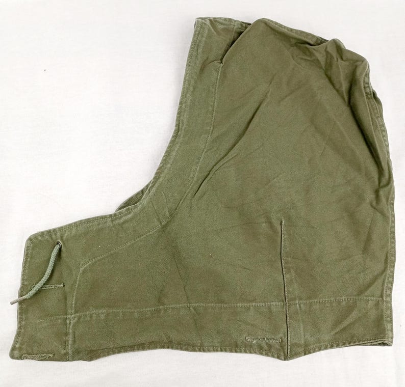 May include: A green canvas hooded jacket with a drawstring closure. The hood is lined with a brown fabric.